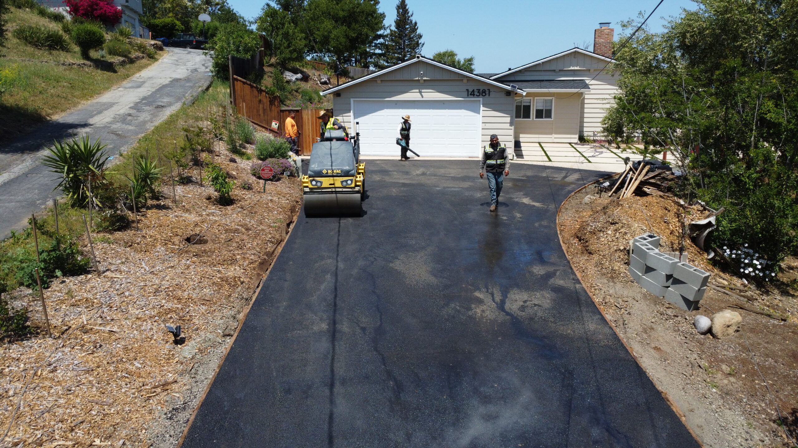 roller compacting the fresh asphalt with the home in the background